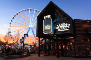 Entrance to Ole Smoky lit up with the wheel at the island and a sunset visible in background. 