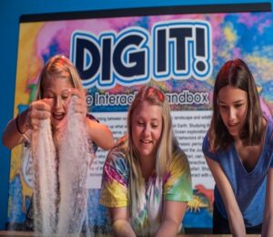 Three girls playing with kinetic sand in a standing sand table