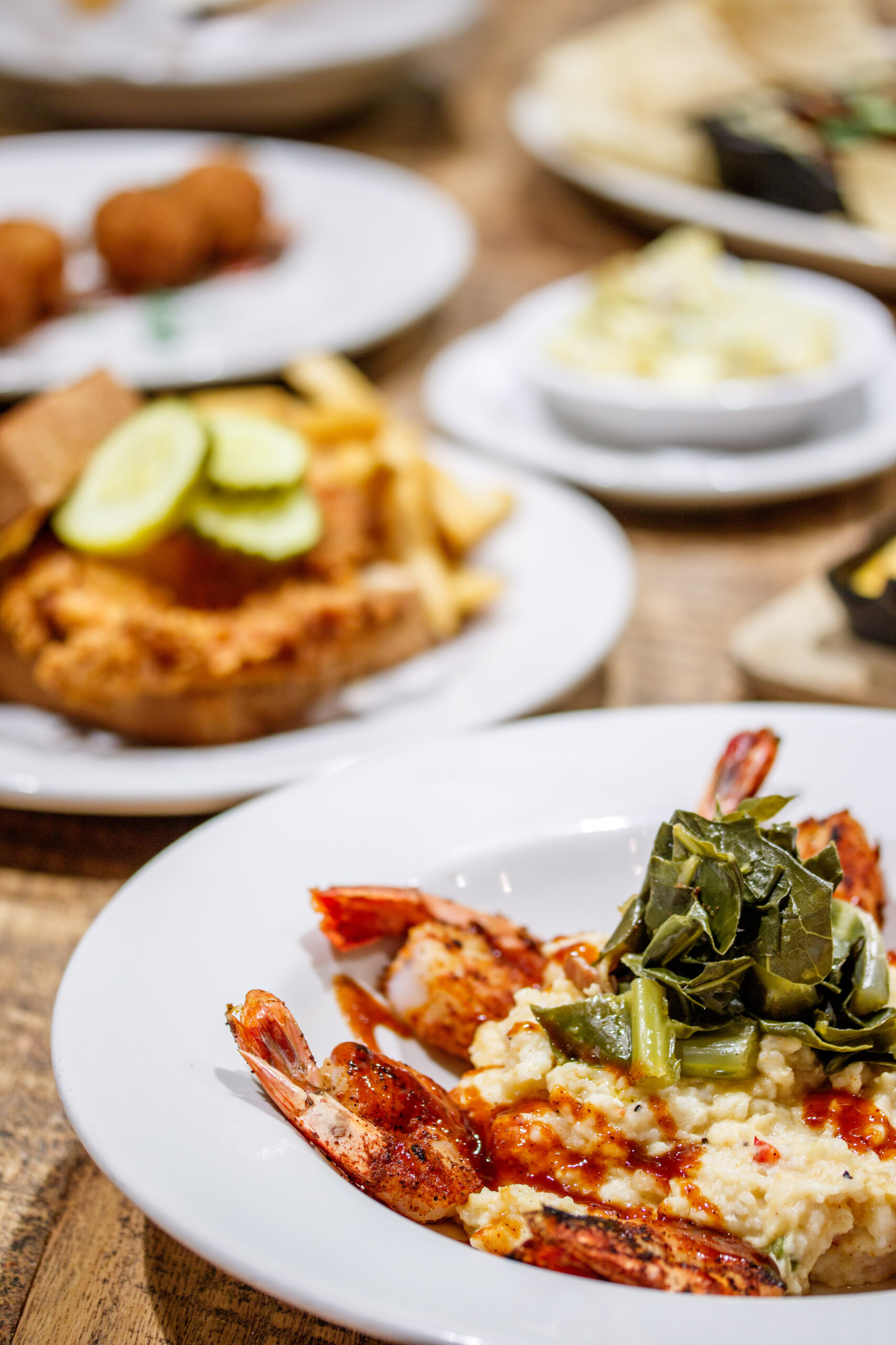 Collard greens piled on a plate of grilled shrimp; Nashville hot chicken visible in the background. 